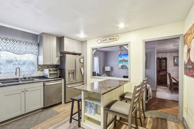 11537 S Neenah Ave, Worth, IL 60482 - kitchen with appliances with stainless steel finishes, a sink, a breakfast bar area, light wood-style floors, and tasteful backsplash