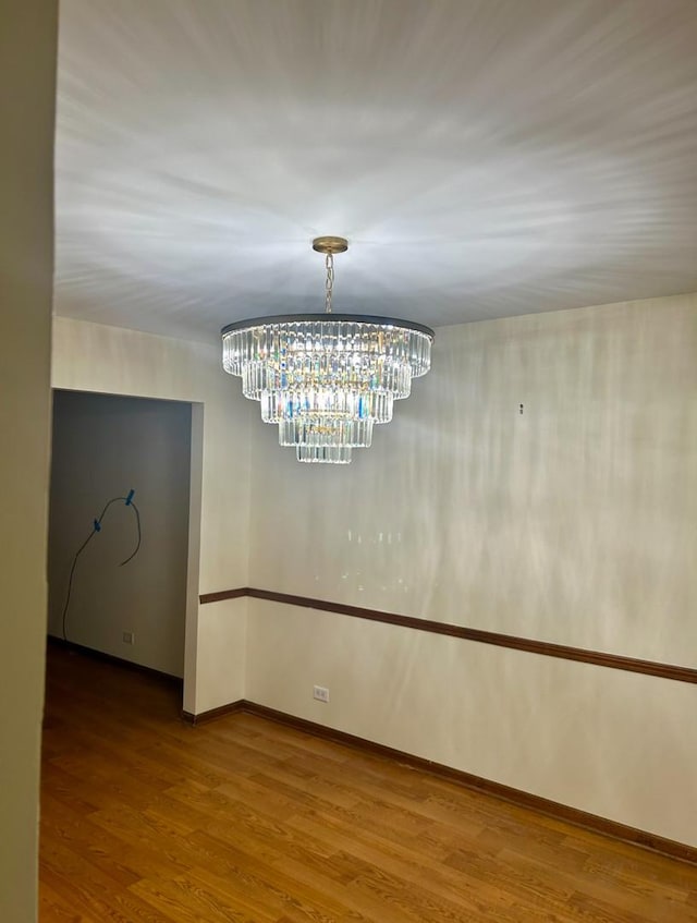 empty room with a chandelier, wood finished floors, and baseboards