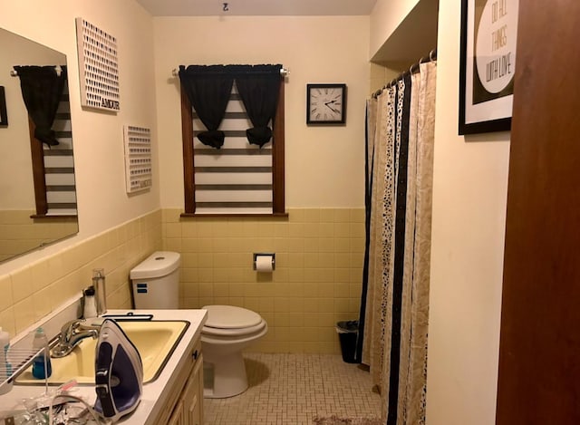 full bath featuring toilet, vanity, wainscoting, tile patterned flooring, and tile walls