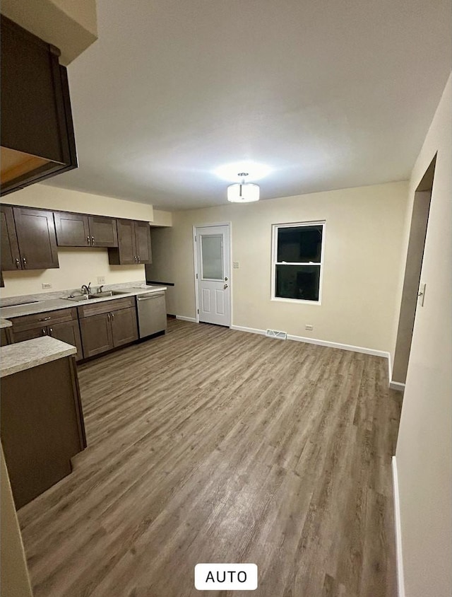 kitchen with light countertops, wood finished floors, dark brown cabinetry, baseboards, and stainless steel dishwasher