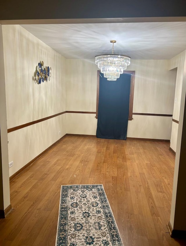 unfurnished dining area with a chandelier, wood finished floors, and baseboards
