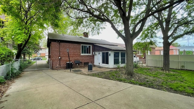 rear view of property with brick siding, a gate, a chimney, and a patio area