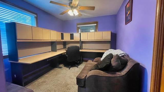 carpeted office space with built in desk and a ceiling fan