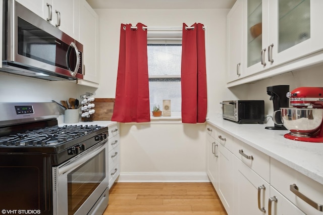 2017 W Farragut Ave Unit 1, Chicago, IL 60625 - kitchen with appliances with stainless steel finishes, light wood-style floors, white cabinets, and glass insert cabinets