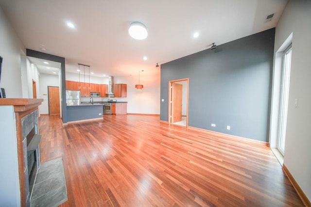 4770 N Manor Ave Unit 405, Chicago, IL 60625 - unfurnished living room with light wood-style floors, a tiled fireplace, a sink, recessed lighting, and baseboards
