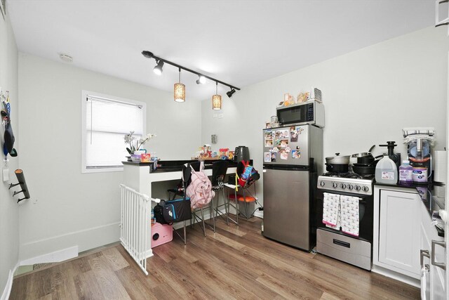 4854 W Addison St, Chicago, IL 60641 - kitchen featuring stainless steel appliances, light wood-style floors, rail lighting, white cabinets, and dark countertops