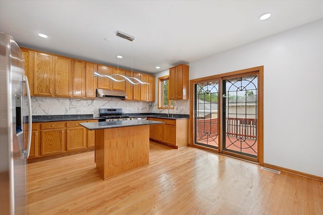 1019 W 47th Pl, Chicago, IL 60609 - kitchen featuring under cabinet range hood, stainless steel appliances, dark countertops, light wood-style flooring, and decorative backsplash