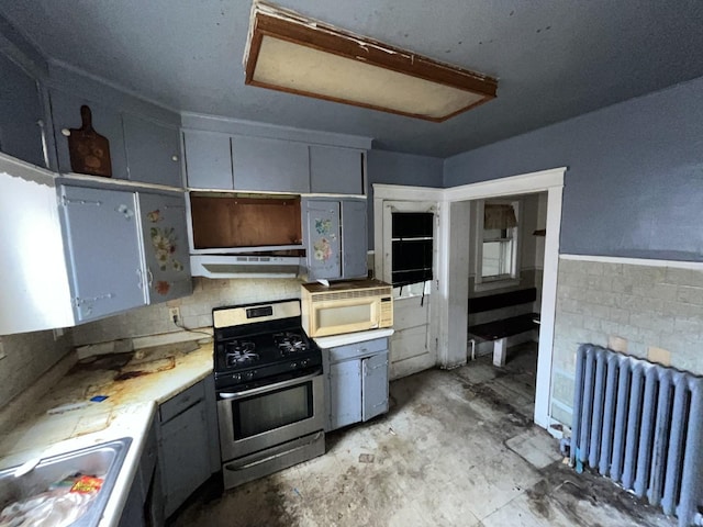 104 Interocean Ave, South Chicago Heights, IL 60411 - kitchen featuring radiator, stainless steel gas range, white microwave, under cabinet range hood, and unfinished concrete flooring