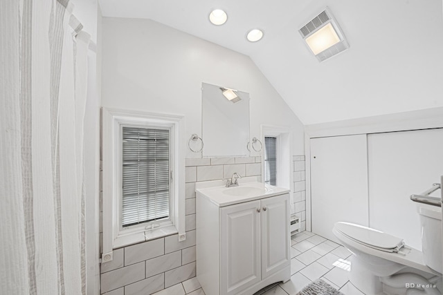 5213 Fairview Ave, Downers Grove, IL 60515 - bathroom featuring lofted ceiling, toilet, vanity, tile patterned floors, and tile walls