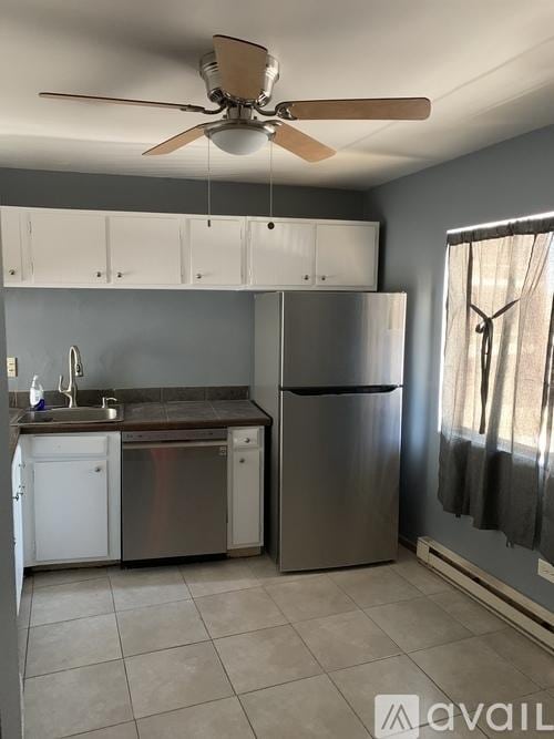 kitchen with stainless steel appliances, a sink, a baseboard radiator, and white cabinets