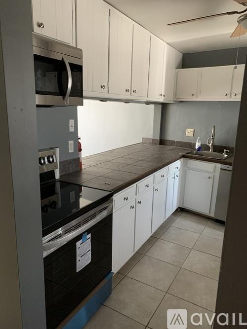 kitchen featuring appliances with stainless steel finishes, white cabinets, light tile patterned floors, ceiling fan, and a sink