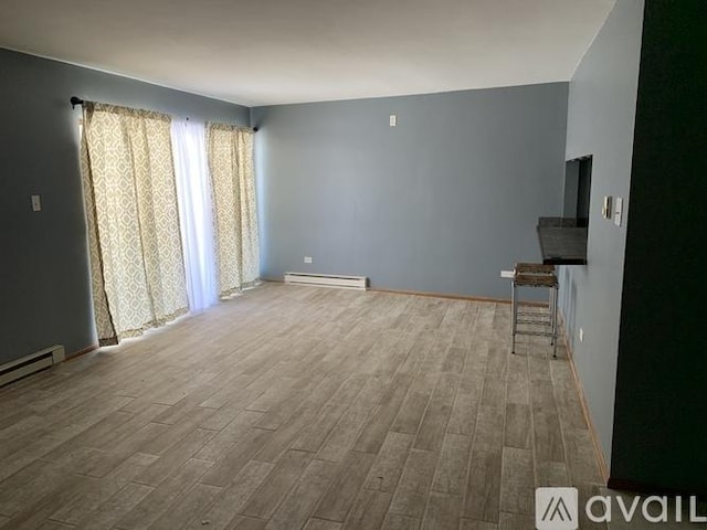 unfurnished living room with a baseboard heating unit, wood finished floors, and baseboards