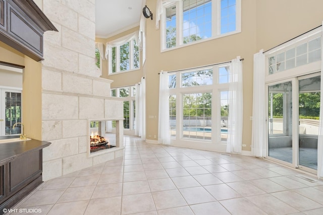 29026 N Brassie Ct, Ivanhoe, IL 60060 - unfurnished living room featuring a high ceiling, light tile patterned flooring, a multi sided fireplace, baseboards, and crown molding