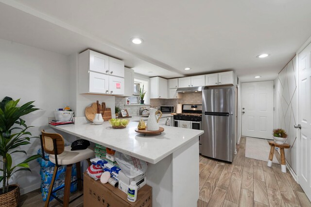 1630 N Avers Ave, Chicago, IL 60647 - kitchen featuring stainless steel appliances, under cabinet range hood, a peninsula, a breakfast bar area, and white cabinets