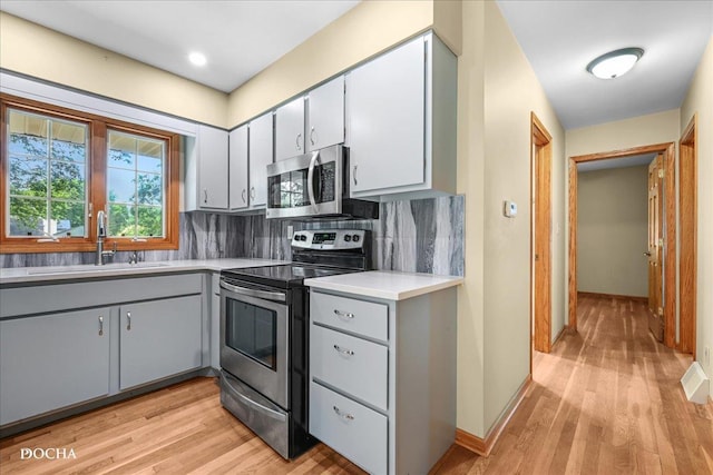 510 W Grant St, Sheridan, IL 60551 - kitchen with appliances with stainless steel finishes, gray cabinetry, light wood-type flooring, and decorative backsplash