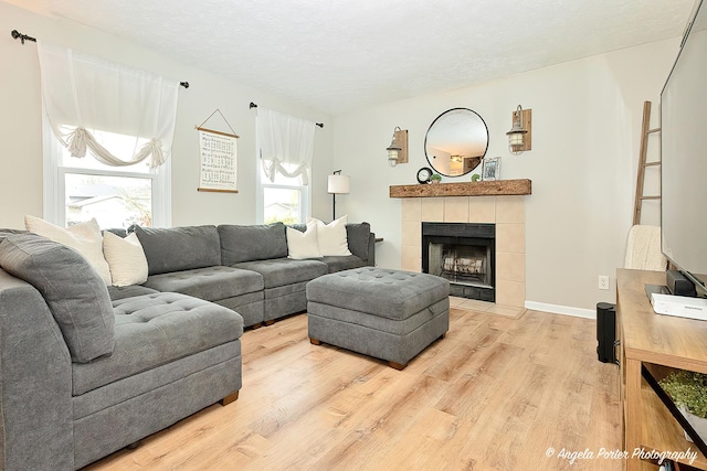 155 Shadowbrook Dr, Capron, IL 61012 - living room with light wood-type flooring, a tiled fireplace, a textured ceiling, and baseboards