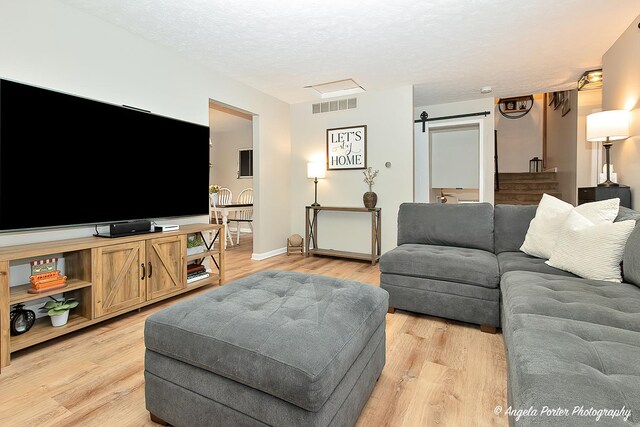 155 Shadowbrook Dr, Capron, IL 61012 - living room featuring a barn door, light wood-style flooring, a textured ceiling, and baseboards