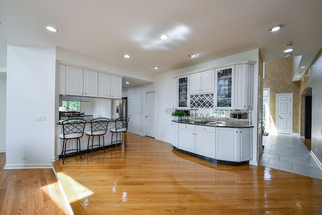 5N311 Lloyd Ave, Itasca, IL 60143 - kitchen with dark countertops, a breakfast bar, glass insert cabinets, light wood-style flooring, and white cabinets