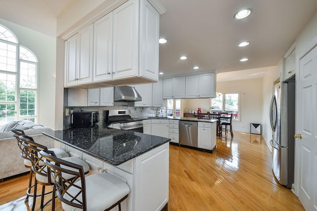 5N311 Lloyd Ave, Itasca, IL 60143 - kitchen featuring appliances with stainless steel finishes, a peninsula, range hood, light wood-style flooring, and white cabinets