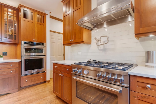 1602 Wickham Ct, Libertyville, IL 60048 - kitchen featuring stainless steel appliances, wall chimney range hood, light countertops, decorative backsplash, and light wood-type flooring