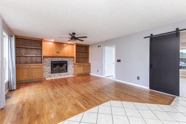 102 Merganser Ct, Downs, IL 61736 - unfurnished living room featuring ceiling fan, a barn door, light wood-type flooring, a stone fireplace, and baseboards