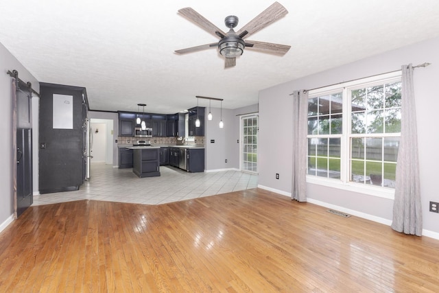 102 Merganser Ct, Downs, IL 61736 - unfurnished living room featuring a barn door, a ceiling fan, baseboards, and light wood-style flooring