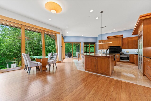515 Stone Ridge Ln, Cherry Valley, IL 61016 - kitchen with appliances with stainless steel finishes, brown cabinets, dark countertops, a kitchen island with sink, and decorative light fixtures
