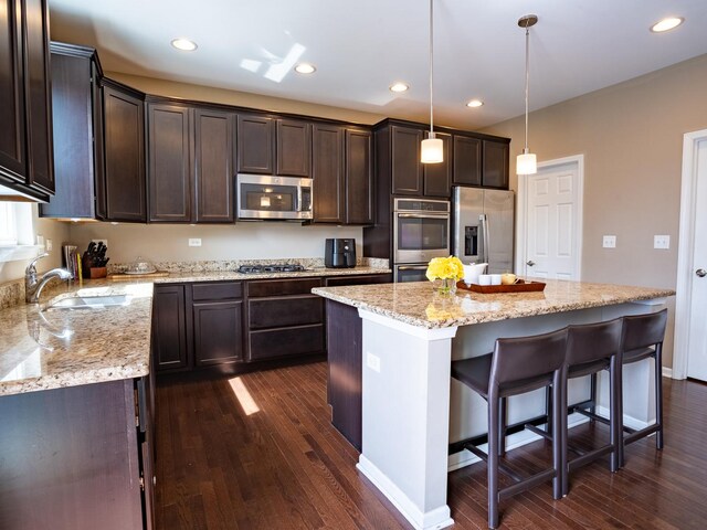 3740 Ryder Ct, Naperville, IL 60564 - kitchen featuring appliances with stainless steel finishes, dark brown cabinetry, dark wood-style flooring, a kitchen breakfast bar, and light stone counters