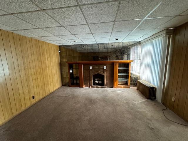 7952 S Elizabeth St, Chicago, IL 60620 - unfurnished living room with wooden walls, radiator, carpet, a brick fireplace, and a paneled ceiling