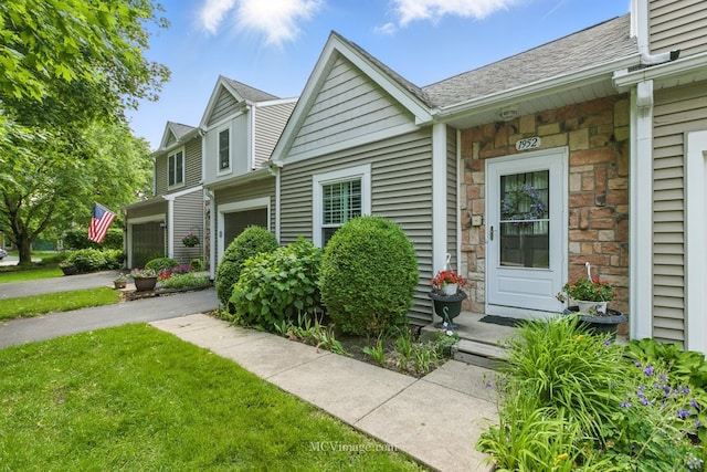 view of front of property with stone siding, a front lawn, and roof with shingles