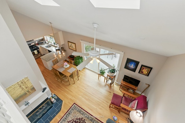 living area featuring a skylight, wood finished floors, vaulted ceiling, and a ceiling fan