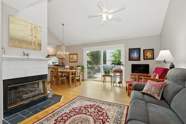 living area featuring wood finished floors, a chandelier, a tile fireplace, ceiling fan, and high vaulted ceiling
