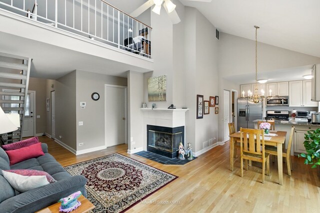 living room with high vaulted ceiling, a ceiling fan, a chandelier, light wood-style floors, and a fireplace