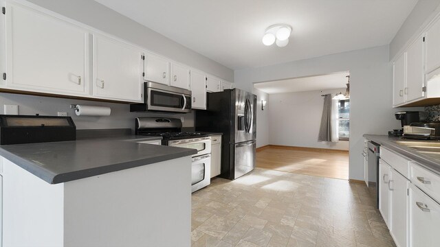 10129 Asbury Ln, Machesney Park, IL 61115 - kitchen featuring stainless steel appliances, white cabinetry, dark countertops, baseboards, and a peninsula
