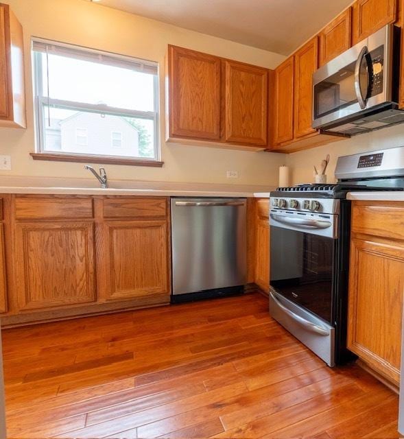 1413 N Metropolitan Ave, Waukegan, IL 60085 - kitchen featuring appliances with stainless steel finishes, light wood finished floors, light countertops, a sink, and brown cabinetry