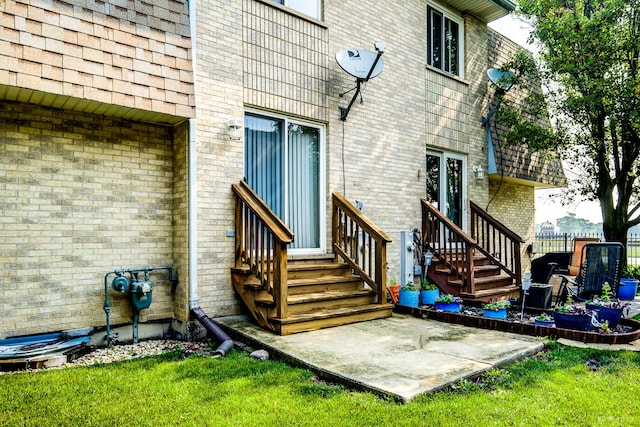 entrance to property with brick siding, a patio area, and a yard