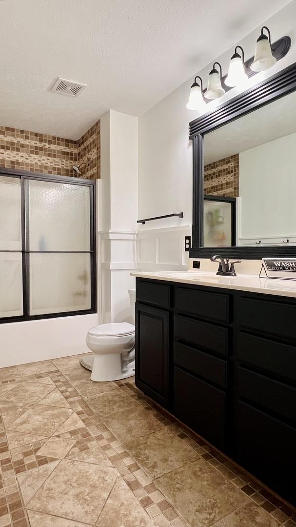 2703 Westbrook Dr, Bloomington, IL 61705 - full bathroom featuring vanity, toilet, bath / shower combo with glass door, and a textured ceiling
