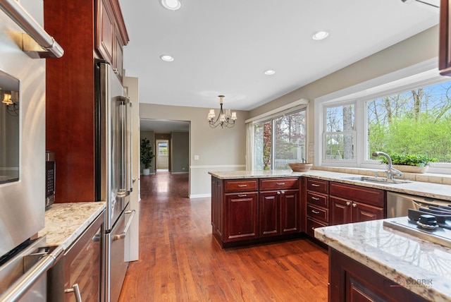 43 Kings Cross Dr, Lincolnshire, IL 60069 - kitchen featuring a sink, a chandelier, reddish brown cabinets, dark wood-type flooring, and light stone countertops