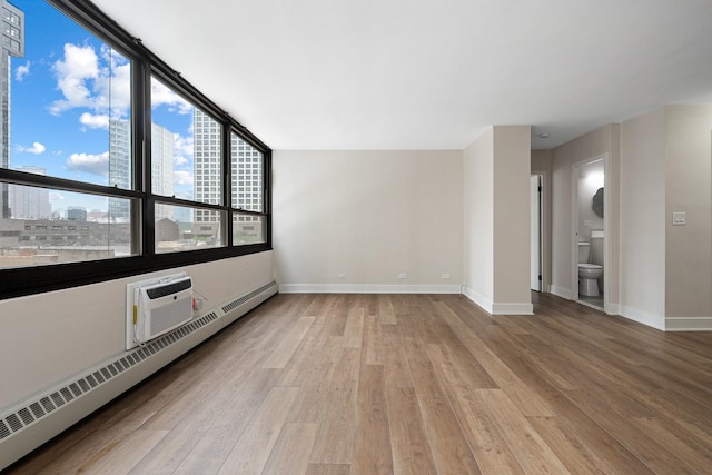 33 E Cedar St Unit 6B, Chicago, IL 60611 - spare room featuring a baseboard radiator, wood finished floors, baseboards, a wall mounted AC, and a city view