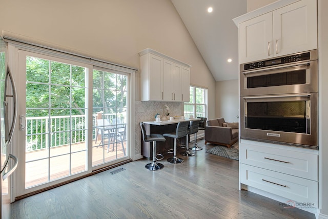 1296 Ashley Ct, Vernon Hills, IL 60061 - kitchen featuring stainless steel double oven, white cabinets, wood finished floors, decorative backsplash, and high vaulted ceiling