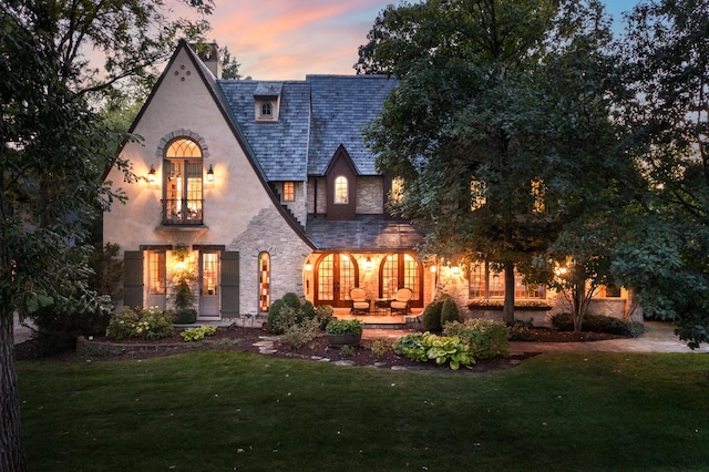 21 Forest Ave, Naperville, IL 60540 - back of house at dusk featuring a high end roof, stone siding, a lawn, a chimney, and a patio area