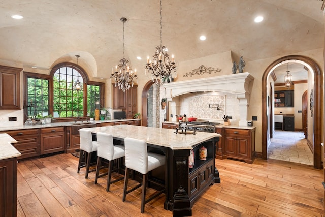 21 Forest Ave, Naperville, IL 60540 - kitchen with arched walkways, vaulted ceiling, a kitchen island, a sink, and light stone counters
