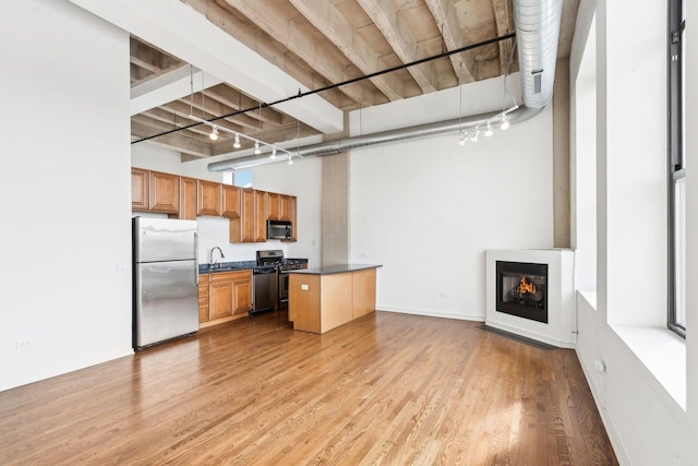 1645 W Ogden Ave Unit 516, Chicago, IL 60612 - kitchen featuring stainless steel appliances, dark countertops, light wood-type flooring, brown cabinetry, and a glass covered fireplace