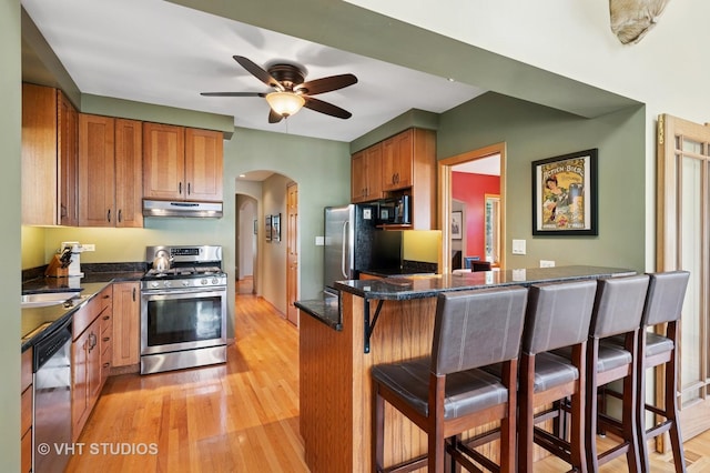 9008 Marmora Ave, Morton Grove, IL 60053 - kitchen featuring appliances with stainless steel finishes, under cabinet range hood, arched walkways, a breakfast bar area, and light wood-type flooring