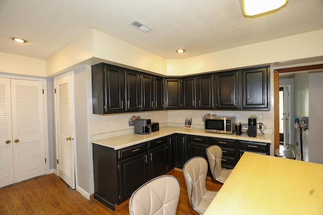 19421 W Hoag Ct, Mundelein, IL 60060 - kitchen with stainless steel microwave, light countertops, wood finished floors, decorative backsplash, and dark cabinetry
