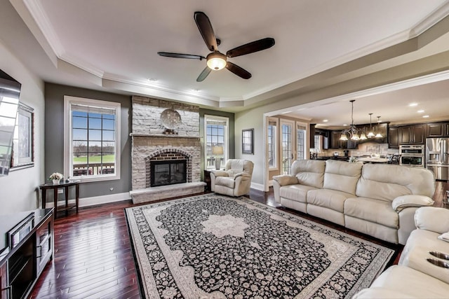 22814 Sara Springs Dr, Frankfort, IL 60423 - living room featuring a ceiling fan, dark wood-style flooring, a stone fireplace, a tray ceiling, and crown molding