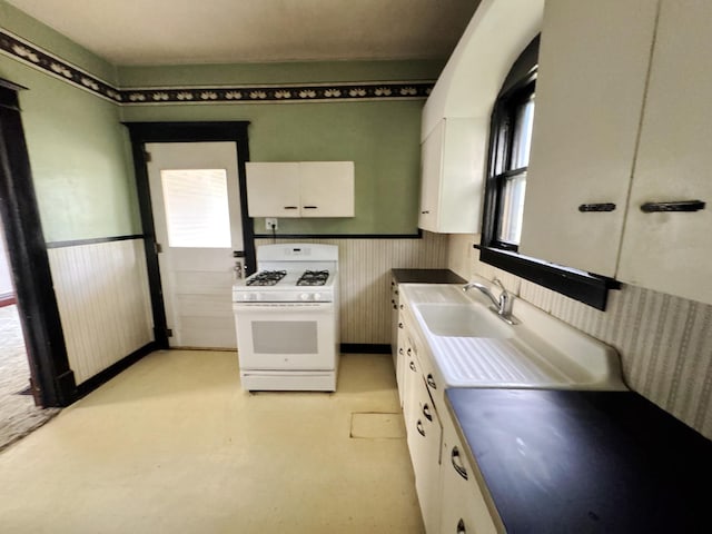 1306 E 4th St, Sterling, IL 61081 - kitchen featuring white gas stove, white cabinetry, a sink, and a wainscoted wall