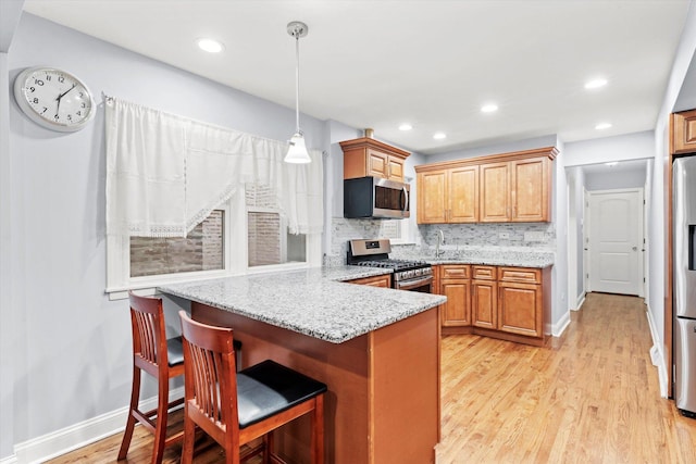 5642 W Dakin St, Chicago, IL 60634 - kitchen with stainless steel appliances, a peninsula, light wood-style flooring, decorative backsplash, and a kitchen bar