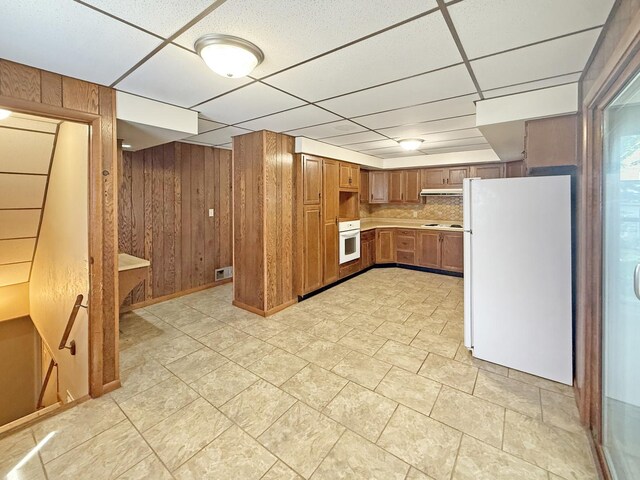 111 E Roosevelt St, Freeport, IL 61032 - kitchen with white appliances, wooden walls, brown cabinets, under cabinet range hood, and a paneled ceiling