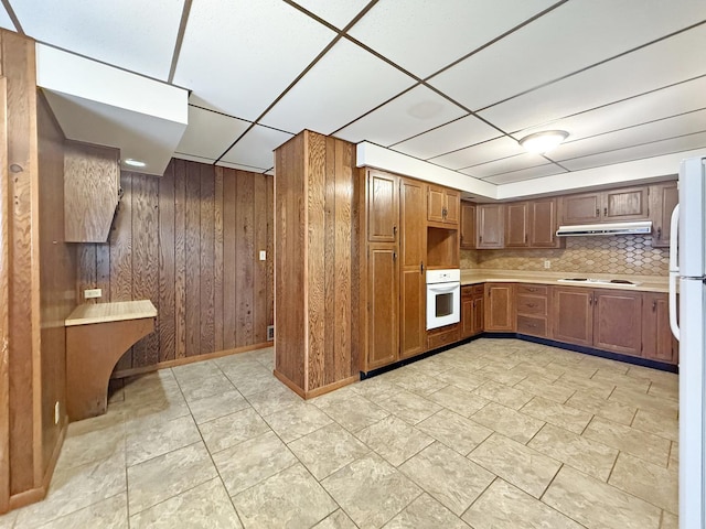 111 E Roosevelt St, Freeport, IL 61032 - kitchen with white appliances, under cabinet range hood, light countertops, brown cabinetry, and wooden walls